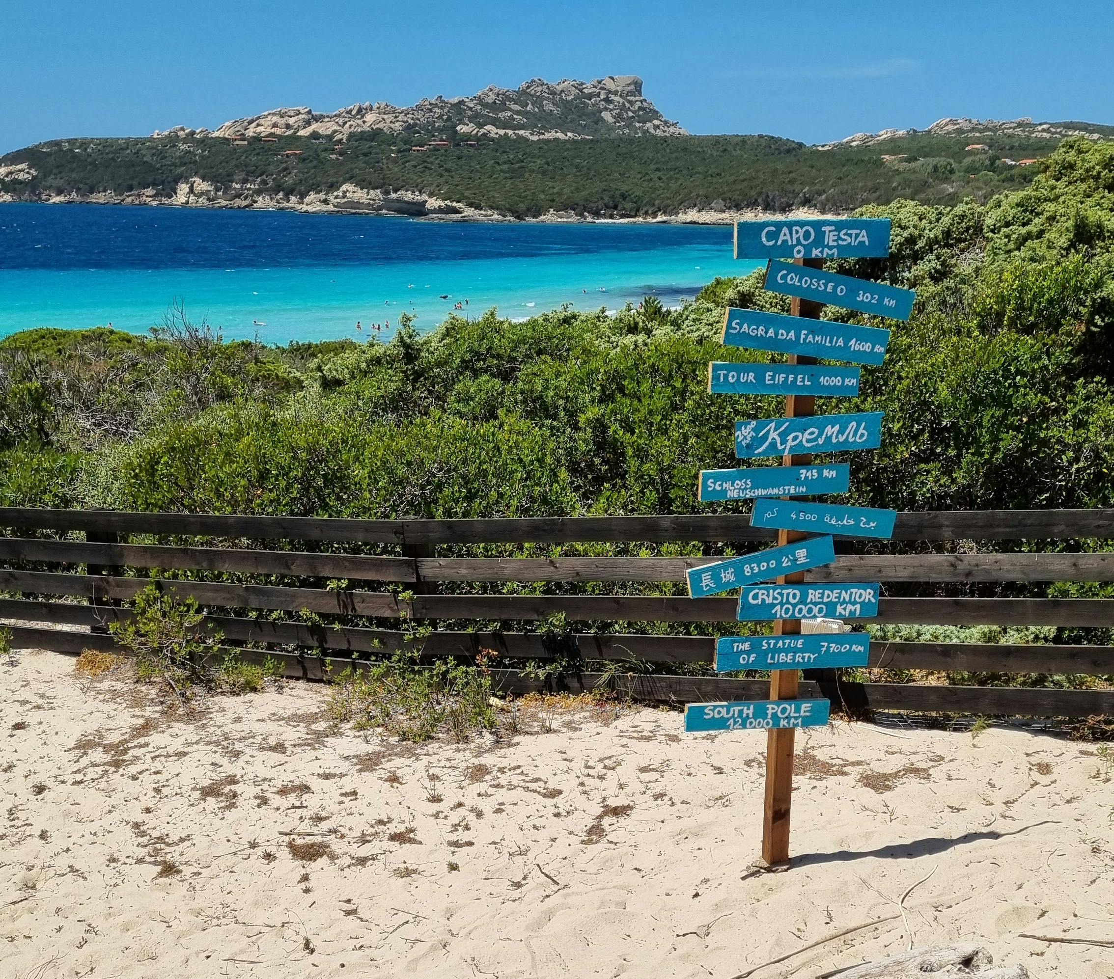 ARCIPELAGO DI LA MADDALENA Beautiful Sardinian beach with a directional signpost pointing to global landmarks.